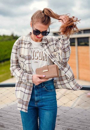 Plaid shirt in beige and brown, white graphic T-shirt, high-waisted blue jeans, and a light brown textured wallet. Accessory: large black sunglasses.