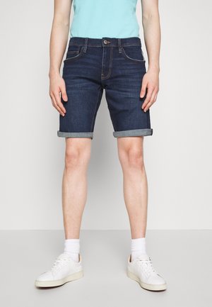 Jeansshorts i mörkblått med uppvikta fållar, har framfickor och knappstängning. Matchas med vita sneakers och ankelsockor.
