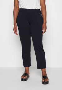 Marineblauwe elastische taillebroek met slanke pasvorm, voorzien van zijzakken en een gladde textuur. Gepaarde met zwarte open-toed sandalen.