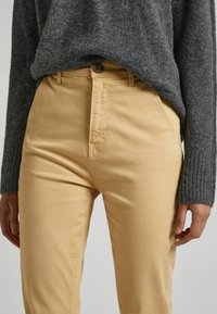 Béžové bavlněné kalhoty s rovný fit, s zipovým zapínáním, knoflíkovým zapínáním v pase a bočními kapsami. Oblečené s šedým pleteným svetr.