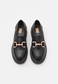 Zwarte leren loafers met een robuuste zool, voorzien van een gouden kettingdetail aan de voorkant en een gestructureerde binnenzool.