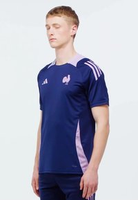 Námornícky športový dres s krátkym rukávom, so svetloružovými akcentmi, okrúhlym výstrihom a logom kohúta na hrudi. Vyrobený z priedušného materiálu.