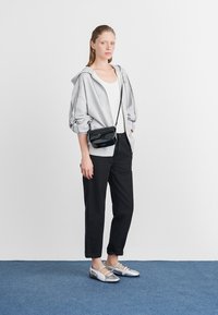 Γκρι oversized hoodie, λευκό tank top, μαύρο tapered παντελόνι και ασημί παπούτσια με λουριά. Μαύρη τσάντα χιαστί. Απλός σχεδιασμός, καθημερινή εμφάνιση.