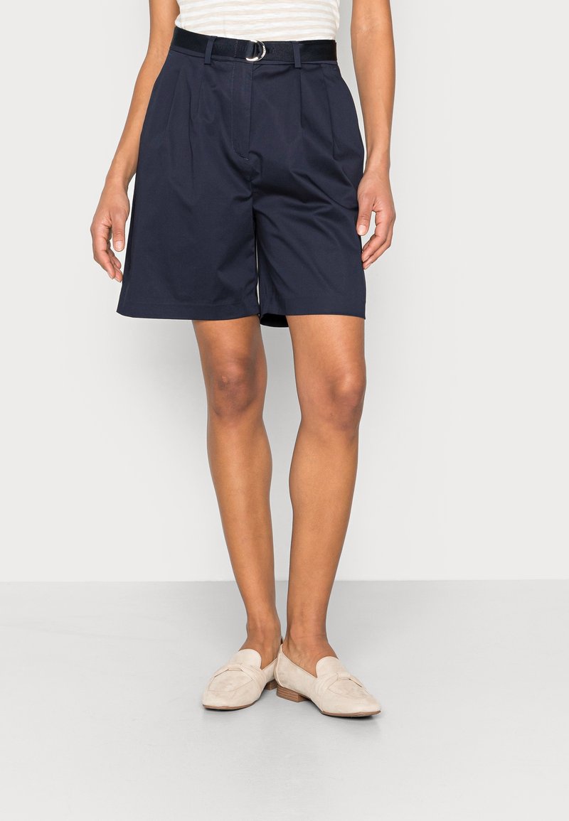 Granatowe plisowane szorty z czarnym paskiem z srebrną klamrą, wykonane z gładkiego materiału. Krótsze niż do kolana, z bocznymi kieszeniami.