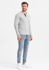 Harmaa pitkähihainen henley-paita, jossa on musta nappilista, yhdistettynä vaaleansinisiin kulutettuihin skinny-farkkuihin ja valkoisiin tennareihin.