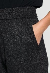 Černé třpytivé tepláky s elastickým pasem, obsahující boční kapsy a měkký, texturovaný povrch.