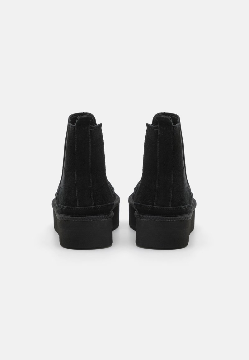 Bottines en suede noir avec une semelle en caoutchouc plate, présentant un design épuré et des tirants à l'arrière visibles pour un enfilage facile.