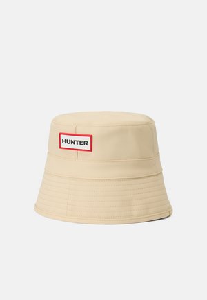 Beige emmerhoed van soepel materiaal met een rood omrand wit label met de tekst "HUNTER". Stiksels rond de rand.