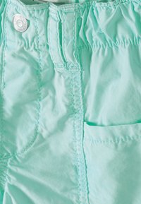 Shorts en bleu clair fabriqués en tissu léger avec une taille élastique, des coutures décoratives et une petite poche latérale. Détail en bouton argenté.
