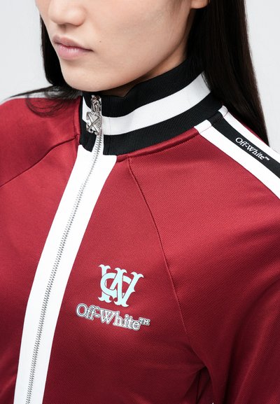 Červená bunda s vysokým límcem, která má bílý zip a kontrastní černobílé pruhy. Obsahuje logo a branding značky Off-White.
