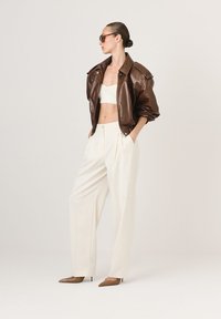 Pruun nahast bomber-jakk, valge crop-top, laiad kreemjad püksid ja pruunid terava ninaosalised kingad. Siledad tekstuurid, struktureeritud disain ja neutraalsed värvid.