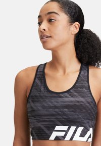 Schwarzes, sportliches Crop-Top mit strukturiertem Muster, kontrastierendem weißen Logo und verstellbaren Trägern. Hergestellt aus dehnbarem Material.