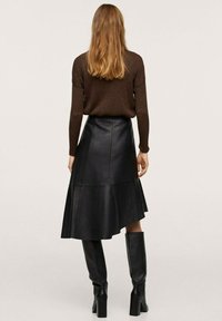 Jupe évasée en cuir noir à taille haute et détails de couture, associée à un haut beige texturé à manches longues et des bottes noires montantes.