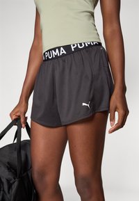 Mustad mustad lühikesed püksid elastse vöökoha ja valge "PUMA" teksti ning kergest kangast, millel on hemil väike valge logo.