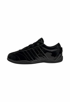 Schwarzer glänzender Sneaker mit niedrigem Schaft, strukturierter Sohle und diagonalen Streifendetails an der Seite, von der Außenseite gesehen.