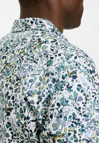 Kurzarmhemd mit weißem Hintergrund und einem mehrfarbigen Blattmuster in Grün- und Blautönen, strukturierter Stoff mit einem steifen Kragen.