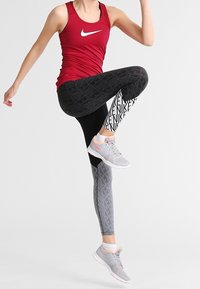 Canotta rossa Nike con logo, leggings neri e grigi con motivo testuale, e scarpe sportive grigio chiaro.