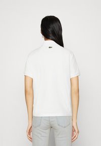 Camisa polo blanca de algodón, con un logo de cocodrilo verde en la parte posterior, mangas cortas y un diseño de cuello clásico.