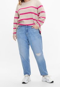 Pull en maille beige avec des rayures roses ; associé à un jean bleu clair déchiré. Il présente une coupe décontractée et des baskets blanches.