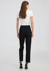 Zwarte tapered broek met een elastische tailleband, gecombineerd met een aansluitend wit shirt met korte mouwen. Glad materiaal, minimalistisch ontwerp.