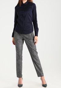 Navyblauwe, lange mouwen overhemd met knopen, gecombineerd met grijs geruite pantalon en groene hakken. Glad materiaal en gestructureerde pasvorm.
