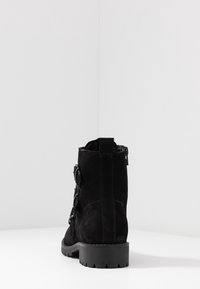 Bottine en daim noir avec une finition texturée, un petit talon carré, une fermeture éclair sur le côté et un détail de matériel de sangle décorative.