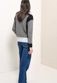 Gestrickter Pullover in Grau mit schwarzen und weißen Akzenten. Verfügt über ein strukturiertes Design, einen gerippten Saum und eine lockere Passform, kombiniert mit Jeans mit weitem Bein.