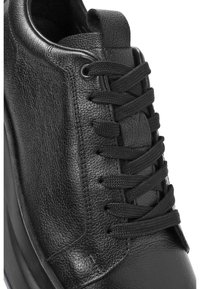 Sneaker in pelle nera con finitura testurizzata, caratterizzato da lacci neri, collo imbottito e un leggero ricamo lungo i lati e la punta.