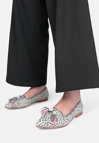 Ballerine con stampa leopardata grigia, decorate con nappine rosa e grigie. Tacco basso in legno marrone; punta rotonda; tomaia in tessuto morbido. Indossate con pantaloni neri.