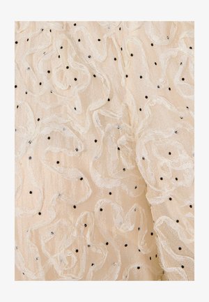 Beige stof met witte kantkrullen en kleine zwarte stippen gelijkmatig verspreid over het oppervlak.