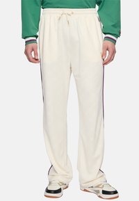 Crème-kleurige sweatpants met een subtiel logo patroon, elastische tailleband, trekkoord en contrasterende paarse zijstrepen.