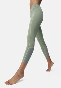 Zöld, magas derekú leggingek érdes szövetből, hálós betétekkel és testhez simuló fazonnal, boka felé szűkülve, lapos varrásokkal.