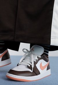 Sneaker bianco e marrone con un logo Nike arancione chiaro, caratterizzato da un esterno in pelle liscia e lacci bianchi, su uno sfondo blu.