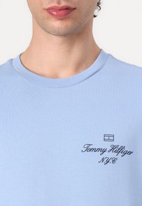 T-shirt en coton bleu clair avec un col rond et un logo sur la poitrine gauche avec "Tommy Hilfiger" et "N.Y.C" en texte noir.