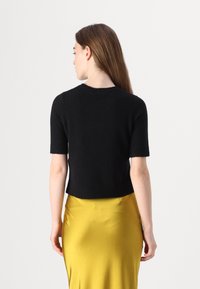 Svart kortermet strikket genser med ribbestrikkede kanter, parret med et blankt gult satengskjørt. Glatt tekstur og tettsittende design.