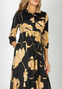 Czarna sukienka z złotymi kwiatowymi wzorami, rękawami do trzech czwartych, spiczastym kołnierzykiem i zwiewną sylwetką. Wykonana z miękkiego, gładkiego materiału.