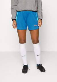 Pantalones cortos deportivos azules con un patrón de diamantes, con detalles en negro y turquesa. Combinados con calcetines blancos y zapatillas deportivas negras.