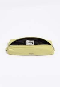 Neceser de color amarillo claro con cremallera, abierto para mostrar un forro interior negro y una etiqueta blanca con "BIMBA Y LOLA" sobre un fondo blanco.