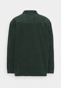 Mörkgrön kordflavourskjorta med krage, långa ärmar och knappdetaljer vid manschetterna. Texturerat ribbat tyg.