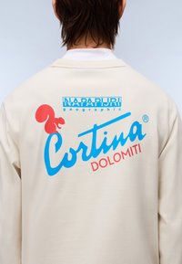 Ανοιχτού μπεζ φούτερ με μεγάλο πολύχρωμο σχέδιο στο πίσω μέρος, που περιλαμβάνει μια σκίουρο, κείμενο και λογότυπο. Μαλακή, άνετη εφαρμογή.