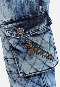 Close-up of blue quilted denim pocket with zipper and button flap on a garment.