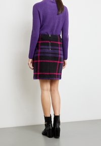 Gonna in misto lana con motivo a scacchi nero e viola, dotata di zip sul retro. Abbinata a un maglione viola a costine e stivaletti neri alla caviglia.