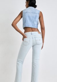 Svetlo modra denim brezrokavnik skrajšane dolžine v kombinaciji s svetlo modrimi širokimi kavbojkami. Ima zadnje žepe s šivi in blagovno oznako na pasu.