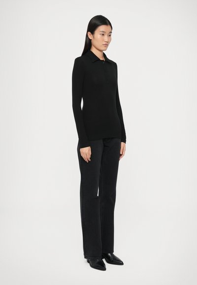 Schwarzes Langarm-Poloshirt mit knöpfbarem Kragen, kombiniert mit schwarzen Jeans mit geradem Bein und schwarzen Stiefeln mit spitzer Spitze.