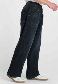 Donkerdenim wijde broek met zijzakken, een ontspannen pasvorm en zichtbare stiksel-details, gecombineerd met witte sneakers.