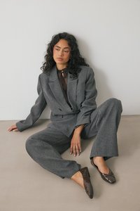 Hall hallikate tekstuuriga ülikond, millel on laiad püksid ja kohandatud bleiser, koos pruunide krokodillimustriga lamejalatsitega ja õhulise pruuni toppiga.