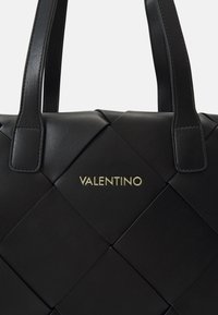 Svart läderhandväska med vävt mönster, utrustad med två robusta handtag och en guld "VALENTINO"-logotyp på den främre panelen.