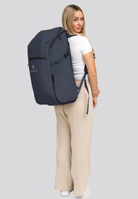 Ampia backpack blu navy con una texture liscia, zip nere e spallacci imbottiti, indossata sulla schiena di una persona in abbigliamento casual.