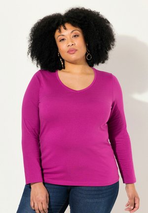 Fuchsia Langarm-Shirt mit V-Ausschnitt aus weichem, glattem Stoff, figurbetontes Design mit leichtem Stretch. Getragen mit dunkelblauen Jeans.