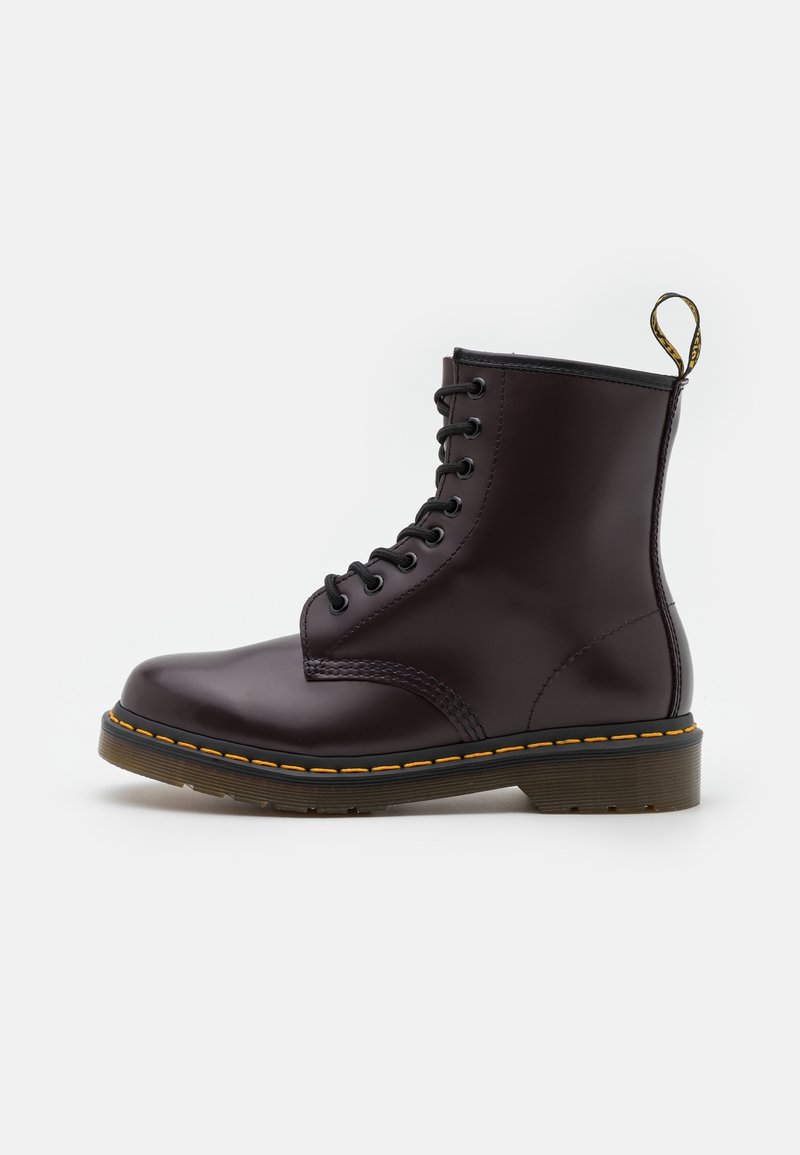Bota de cuero lustrada color marrón oscuro con cordones, suela gruesa translúcida y costuras amarillas, que presenta una pestaña para el talón con la marca.